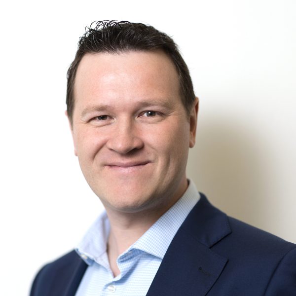 An image of Joel Topham wearing a black jacket with a blue shirt.