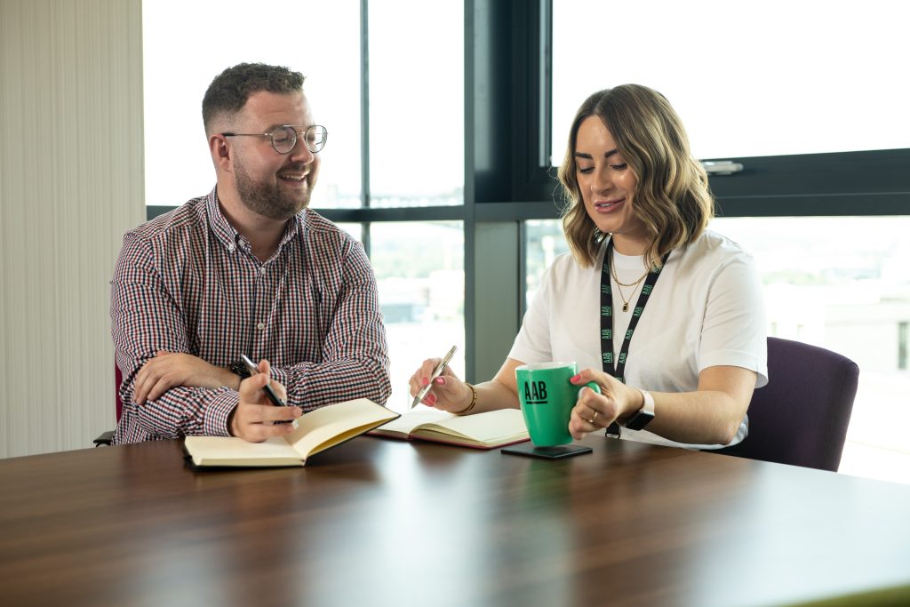 Man and woman working at AAB smiling and writing in notebooks