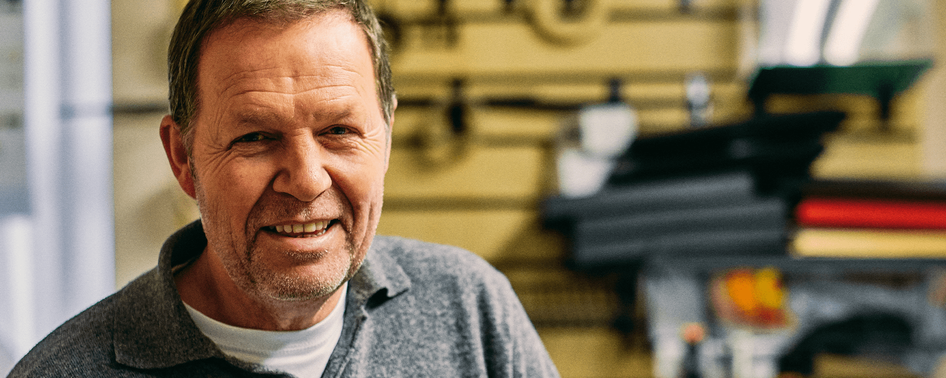 An image of a man wearing a grey jumper and smiling.