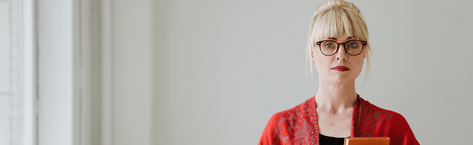An image of a woman wearing a red blazer, black top and black glasses. She is holding documents in her hand. Local tax accountants in scotland banner