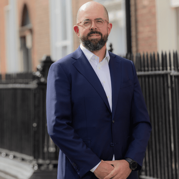 An image of Conor Ryan standing outside with his hands together and smiling at the camera.