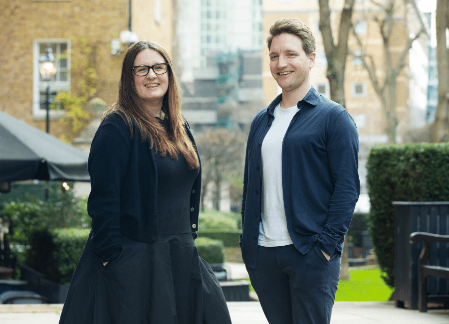 An image of Lauren McCluskey, Sam Wilkinson standing outside and smiling at the camera. Lauren is wearing a black dress and Sam is wearing a blue shirt and white tshirt.