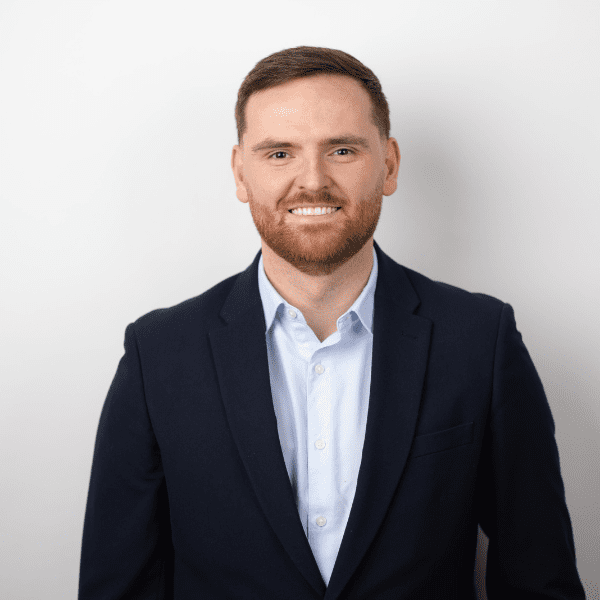 A headshot image of Ronan Dunne. Wearing a black suit jacket and blue shirt.