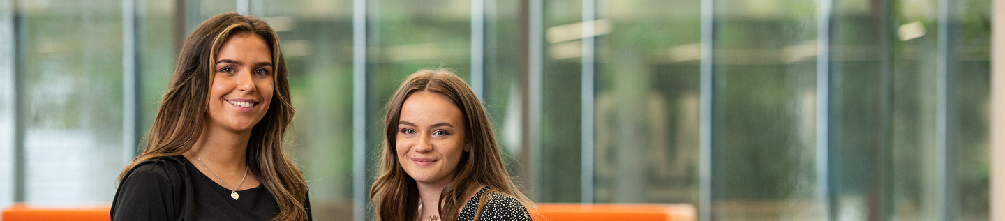 An image of two AAB girls standing in the office and smiling at the camera.